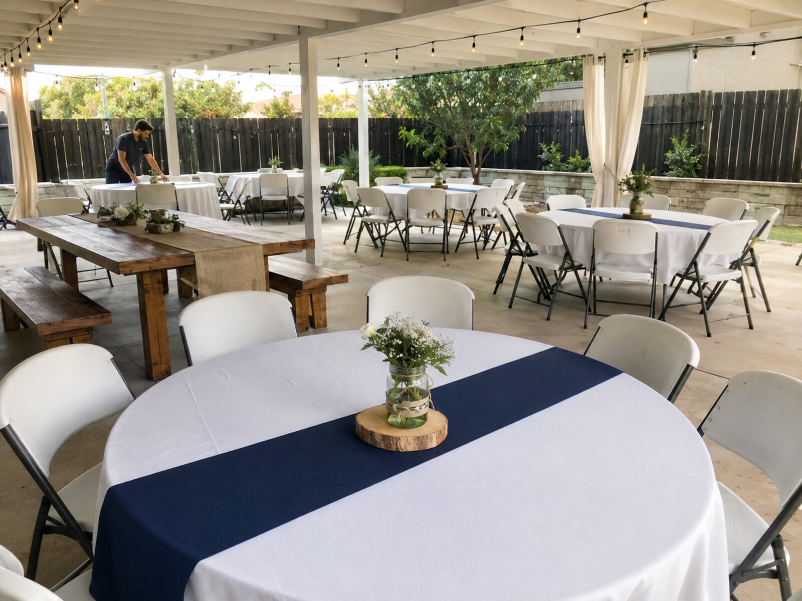 Round rental tables with white linens, navy runners and folding chairs on a patio