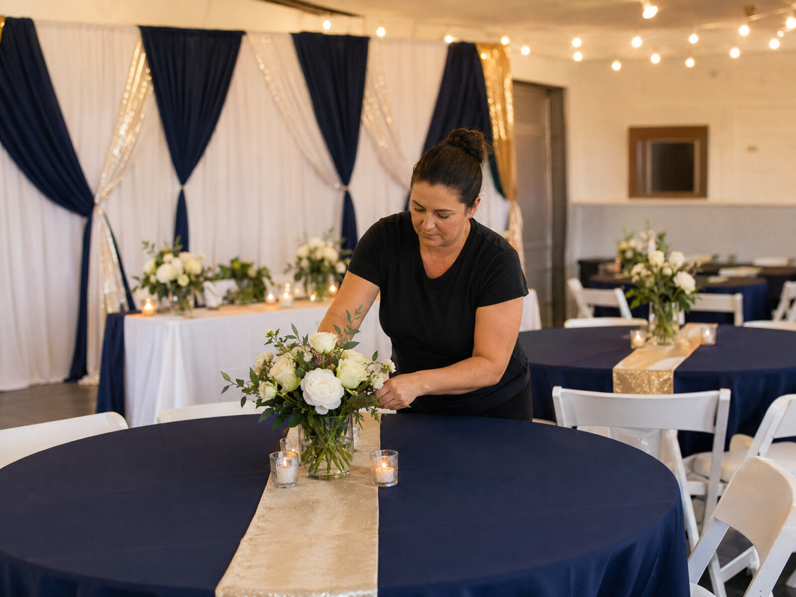 Event décor setup with navy linens, gold runners, candles and floral centerpieces